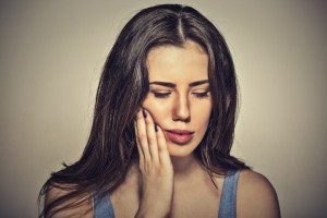 Closeup portrait young woman with sensitive toothache crown problem about to cry from pain touching outside mouth with hand isolated on gray background. Negative human emotion face expression feeling