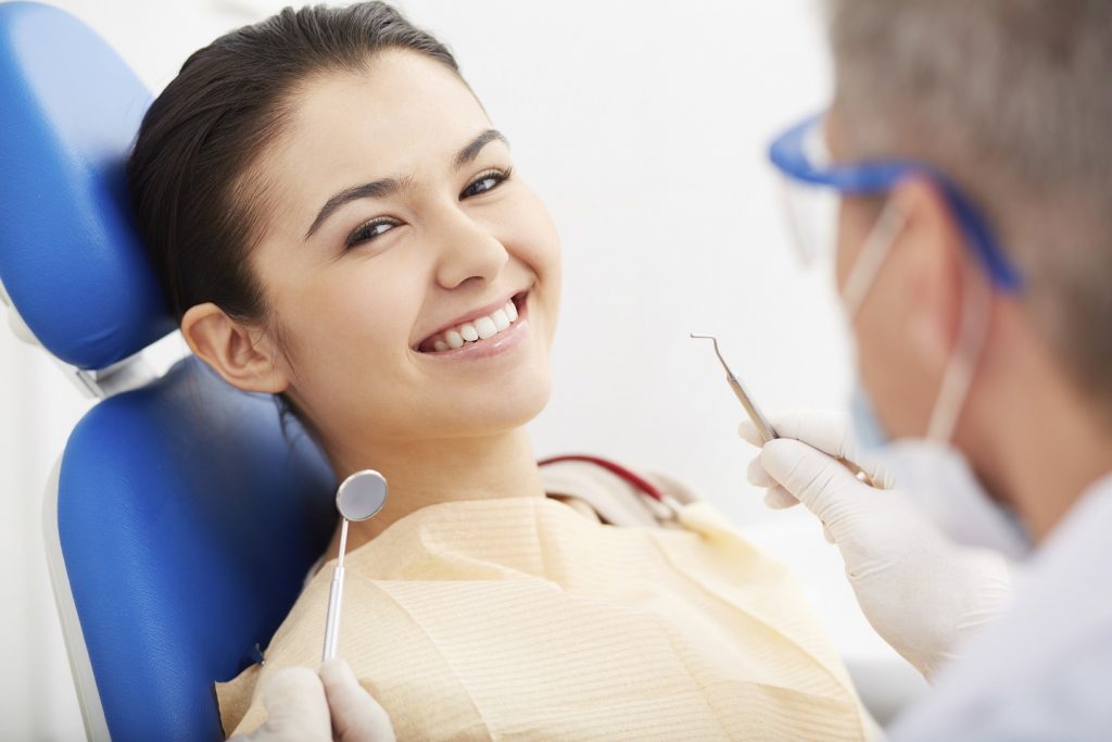 Woman smiles as dentist checks her teeth