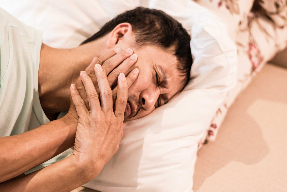 Man in bed winces as his teeth hurt