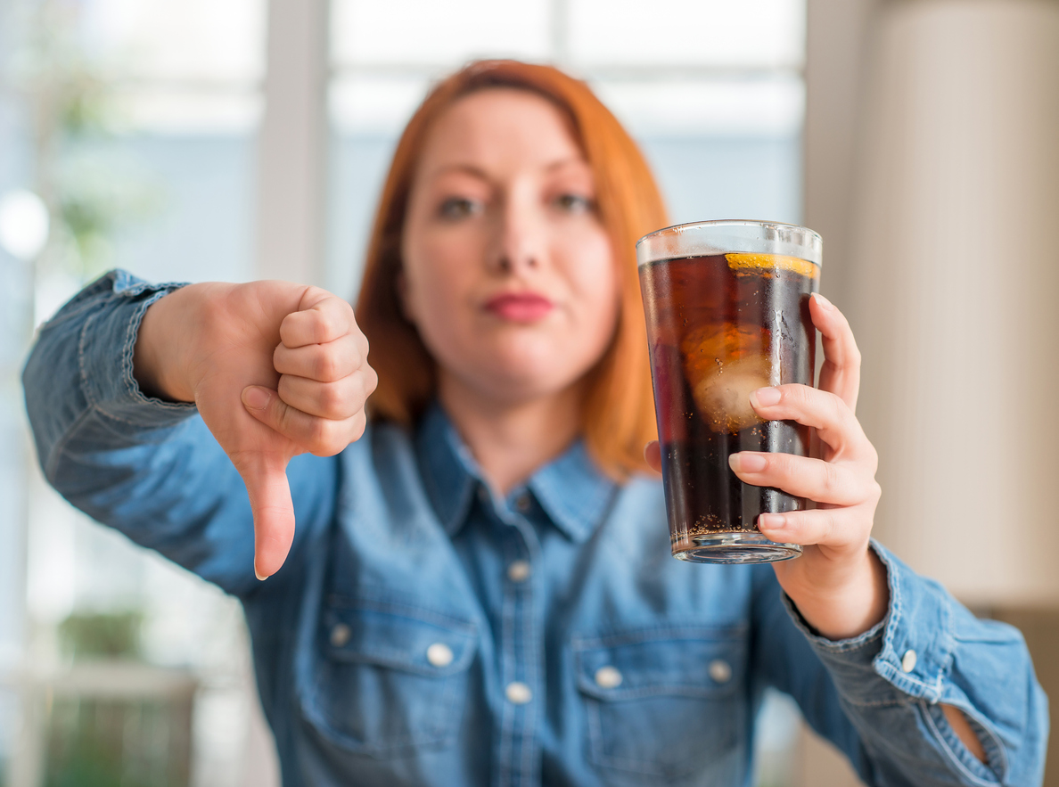 Angry woman holding a soda giving a thumbs down