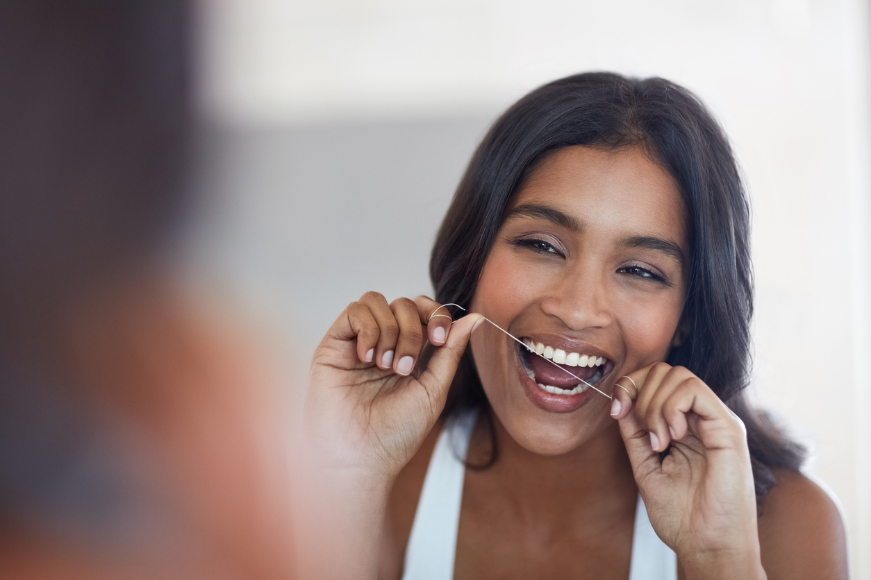 Woman flossing her teeth looking into mirror