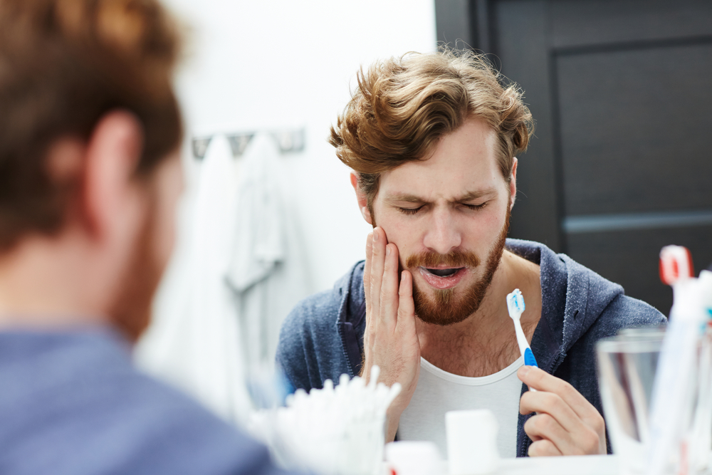 Man feeling toothache while brushing teeth