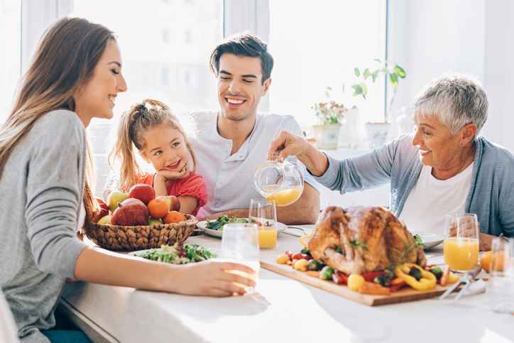 Happy multi-generation family sitting at the dining table with roasted turkey, salad and drinks