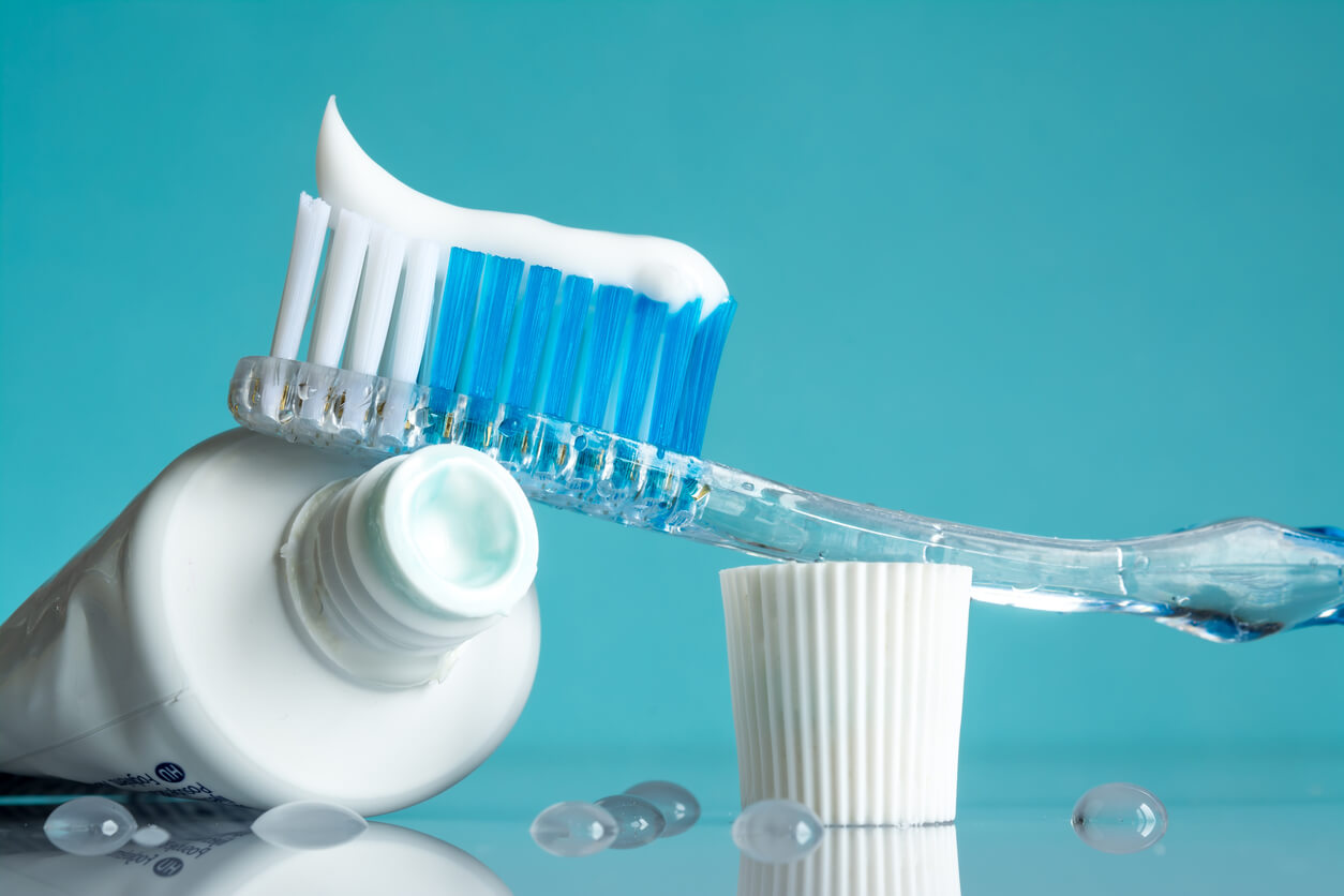 New toothbrush with toothpaste close-up in the bathroom on a mirror table with water drops on a blue background in the sunlight