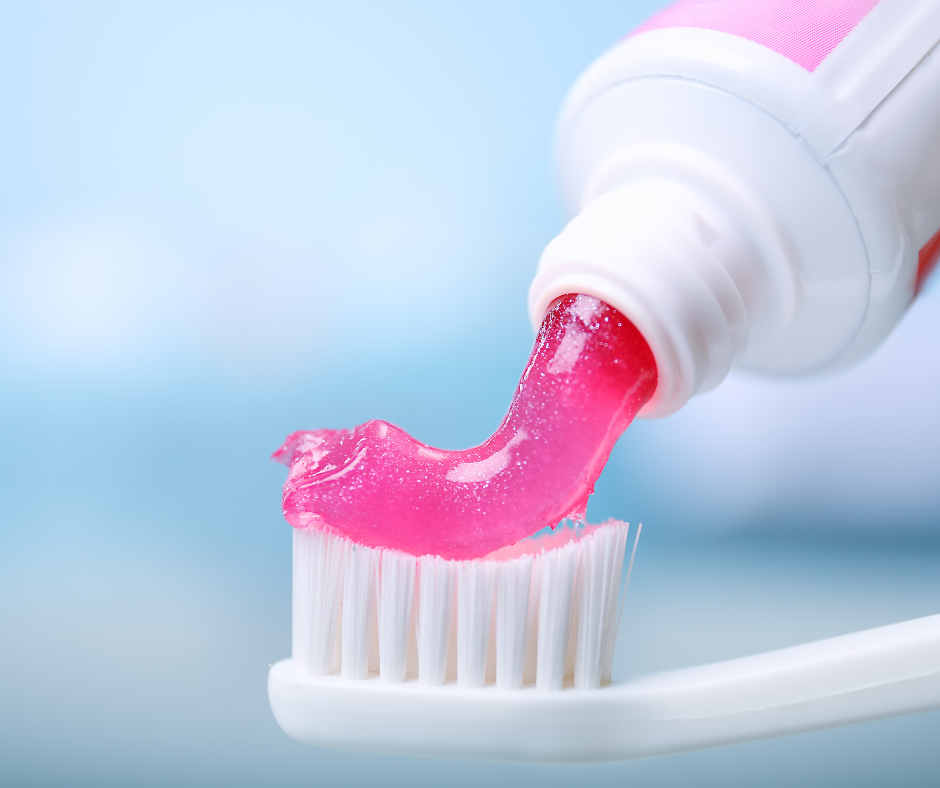 Someone squeezing pink toothpaste on a toothbrush